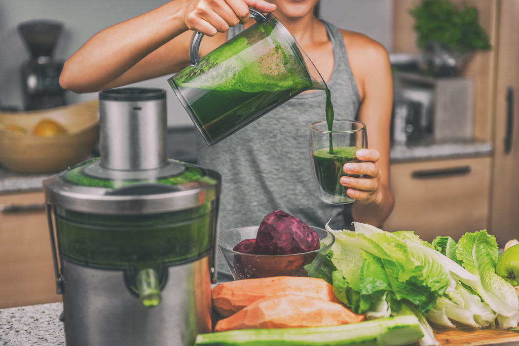 Pessoa servindo num copo de vidro suco verde com alimentos saudáves sobre uma mesa fazendo alusão aos alimentos saudáveis que desincham o corpo